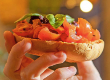 A hand holding Friselle with Fresh tomatoes and basil, typical Puglia apetizer